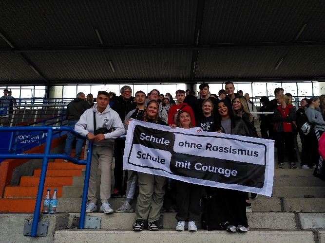 Gruppenfoto der Teilnehmenden Schüler:innen und Lehrer:innen im Stadion des VFL-Bochum mit der Schule ohne Rassismus - Schule mit Courage Fahne